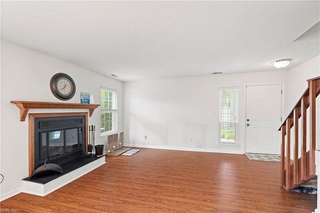 unfurnished living room with wood finished floors, a glass covered fireplace, stairs, and baseboards