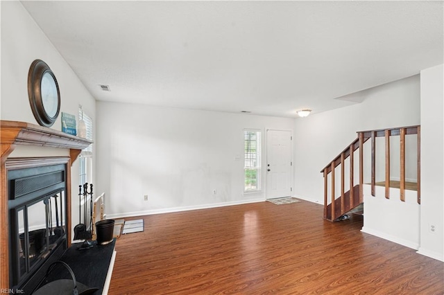 unfurnished living room featuring wood finished floors, stairs, a fireplace with raised hearth, and baseboards