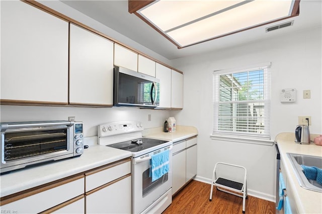 kitchen featuring white electric range, stainless steel microwave, white cabinetry, wood finished floors, and light countertops