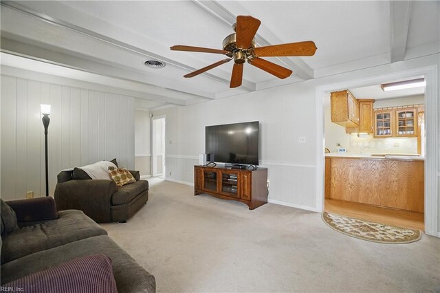 living room featuring ceiling fan, visible vents, beamed ceiling, light carpet, and a decorative wall