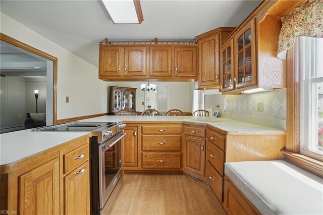 kitchen with glass insert cabinets, light wood-type flooring, light countertops, brown cabinets, and stainless steel range