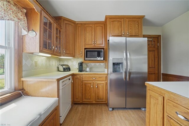 kitchen featuring appliances with stainless steel finishes, light wood-style floors, light countertops, brown cabinetry, and glass insert cabinets