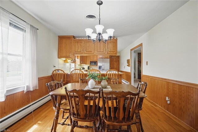 dining space featuring a wainscoted wall, a baseboard heating unit, wood walls, and a notable chandelier