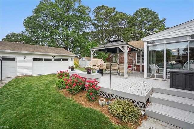 wooden deck featuring a garage, a lawn, an outbuilding, a gazebo, and a storage shed