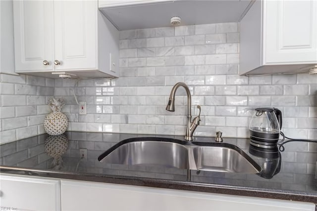 kitchen with a sink, backsplash, dark stone countertops, and white cabinetry