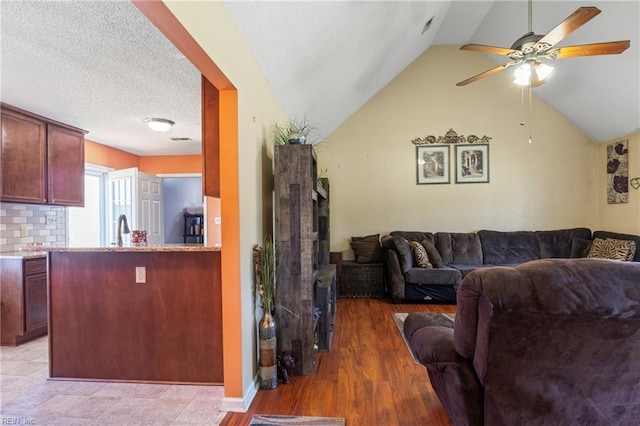 living area with lofted ceiling, a fireplace, light wood-style floors, ceiling fan, and a textured ceiling