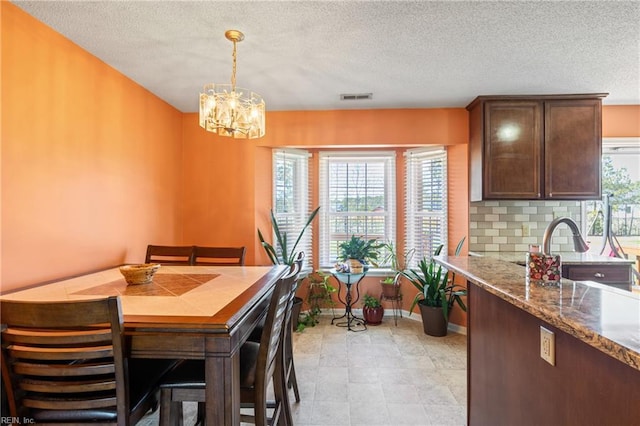dining space featuring visible vents, a textured ceiling, baseboards, and a notable chandelier