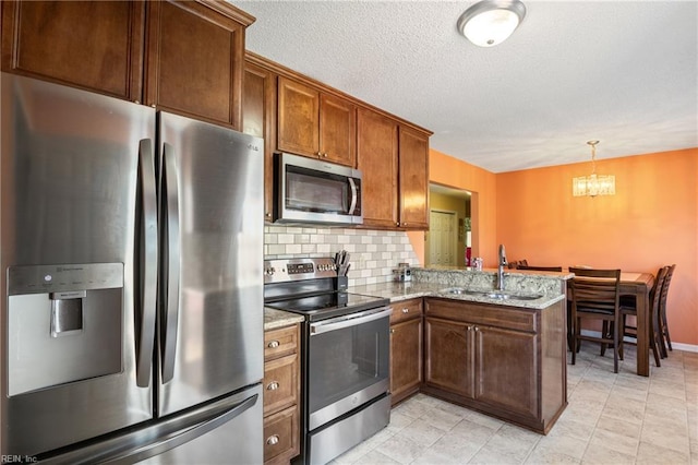 kitchen featuring backsplash, a sink, a peninsula, a notable chandelier, and stainless steel appliances