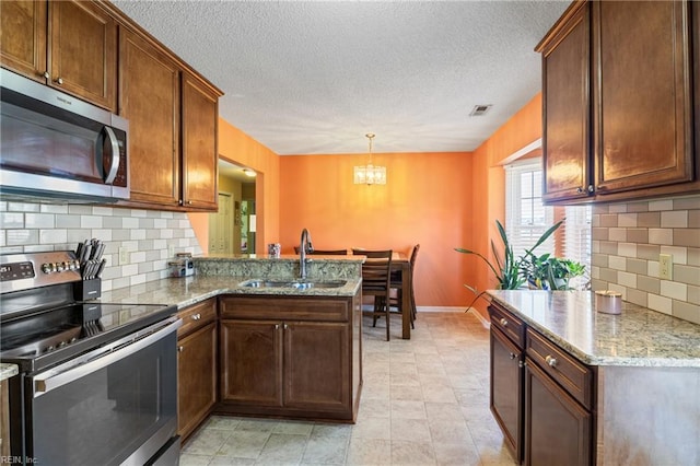 kitchen with a sink, a chandelier, stainless steel appliances, a peninsula, and backsplash