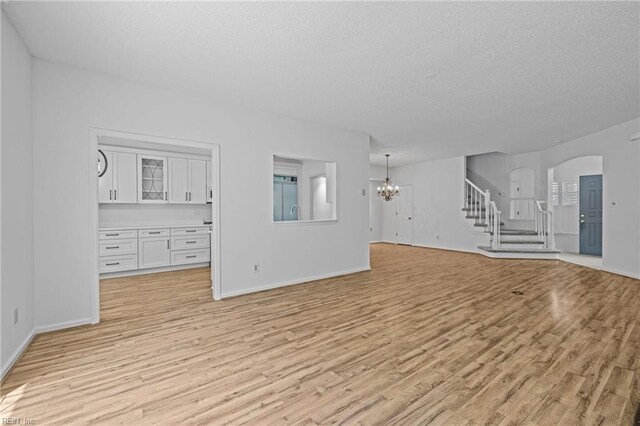unfurnished living room featuring light wood-type flooring, a textured ceiling, a chandelier, and stairway