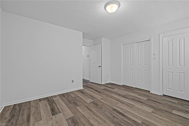 unfurnished bedroom featuring a textured ceiling, baseboards, a closet, and wood finished floors