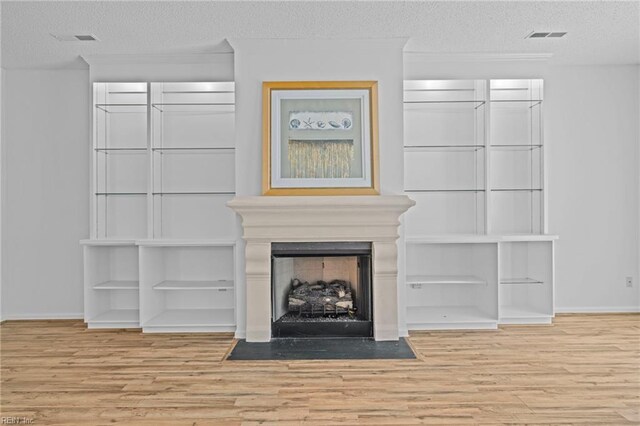 unfurnished living room featuring a fireplace with flush hearth, a textured ceiling, baseboards, and wood finished floors