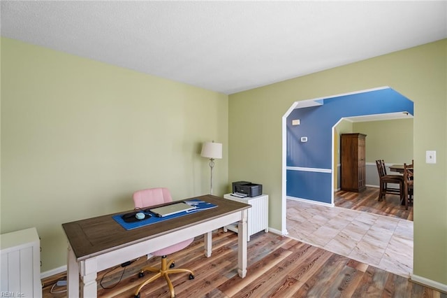 office featuring arched walkways, baseboards, wood finished floors, and radiator