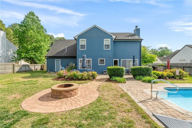 rear view of property with a fenced backyard, a chimney, a patio area, a yard, and a fire pit