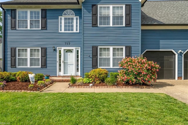 colonial home featuring a garage, driveway, and a front lawn