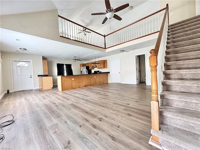 unfurnished living room featuring high vaulted ceiling, a ceiling fan, stairs, and light wood-style flooring