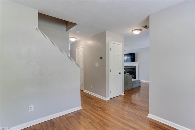 empty room with visible vents, stairs, wood finished floors, a fireplace, and baseboards