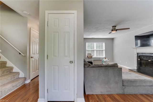 living area featuring stairs, wood finished floors, a fireplace, baseboards, and ceiling fan