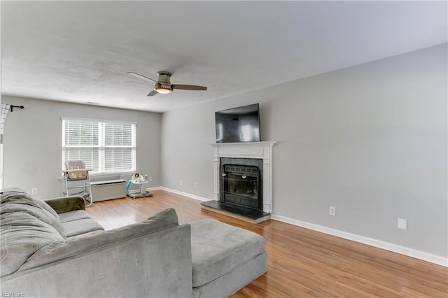 living room with a ceiling fan, baseboards, a fireplace with raised hearth, and wood finished floors