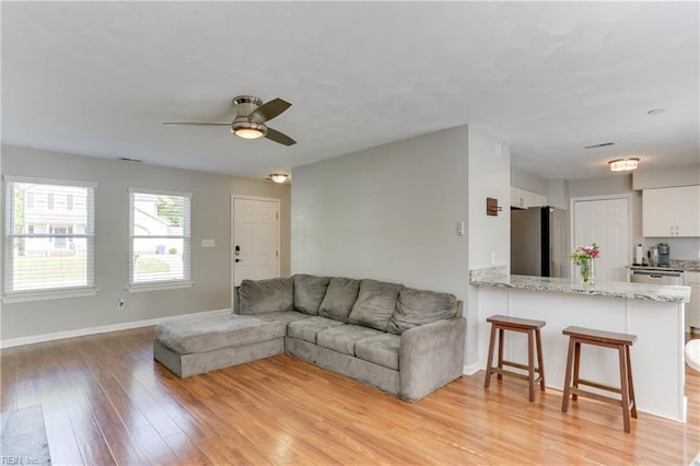 living room with baseboards, a ceiling fan, and light wood-style flooring