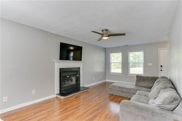 living area featuring baseboards, a ceiling fan, light wood-style flooring, and a fireplace with raised hearth