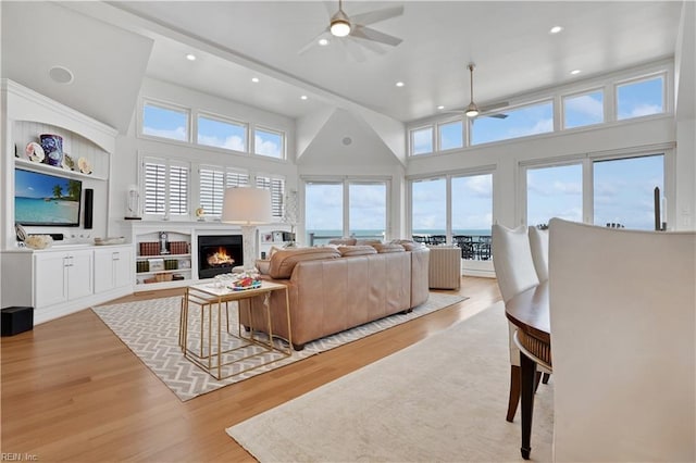 living area with recessed lighting, light wood finished floors, ceiling fan, and a warm lit fireplace