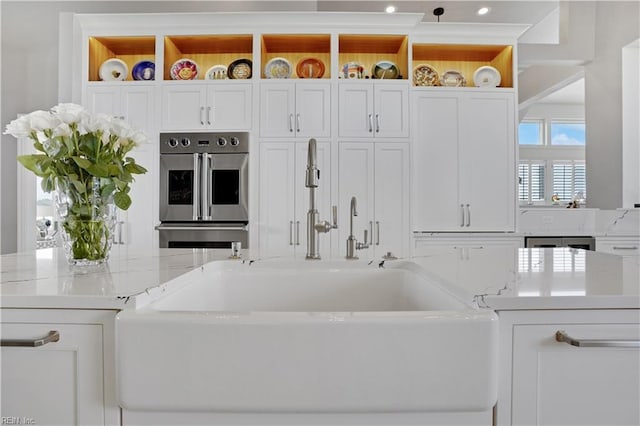interior space with light stone countertops, open shelves, a sink, double oven, and white cabinetry