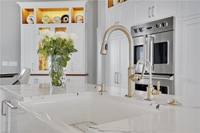 details featuring a sink, white cabinetry, and light stone countertops