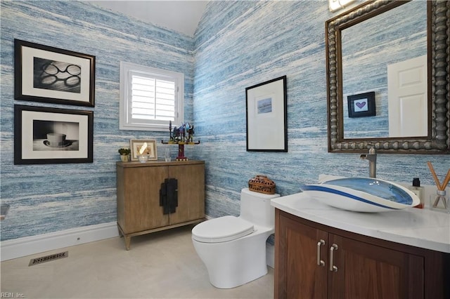 bathroom featuring visible vents, baseboards, vanity, toilet, and wallpapered walls