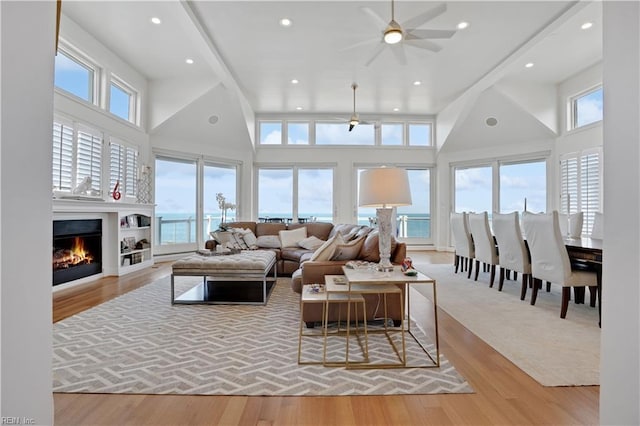 living room with a healthy amount of sunlight, recessed lighting, a high ceiling, and a warm lit fireplace