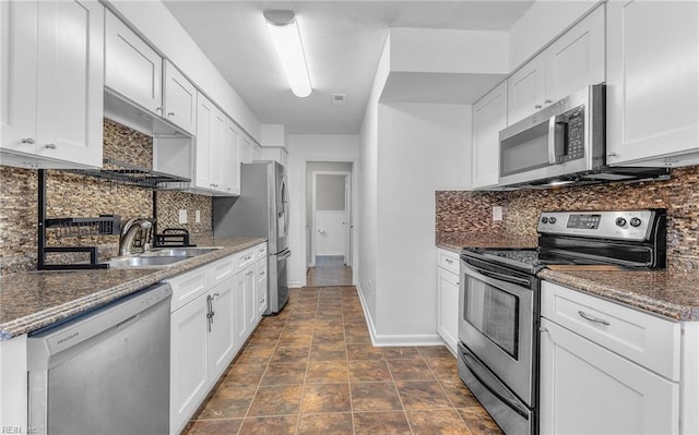 kitchen with a sink, stainless steel appliances, baseboards, white cabinetry, and backsplash