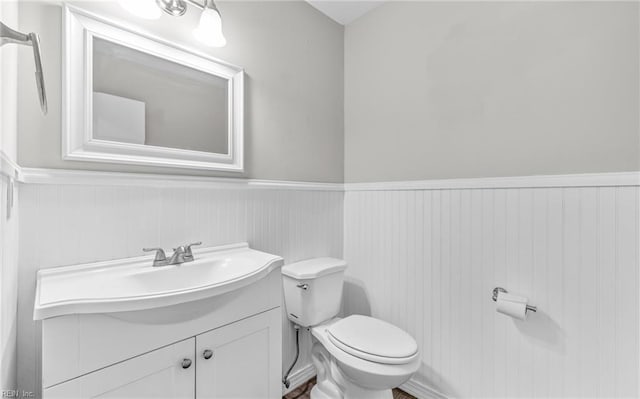 half bathroom with vanity, wainscoting, and toilet