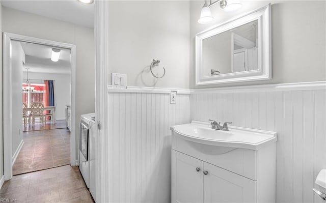 bathroom featuring washer and dryer, vanity, tile patterned flooring, and a wainscoted wall