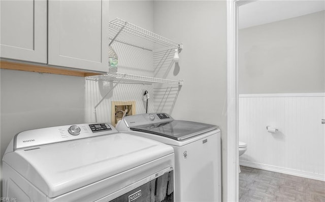 washroom featuring washing machine and clothes dryer, cabinet space, and a wainscoted wall