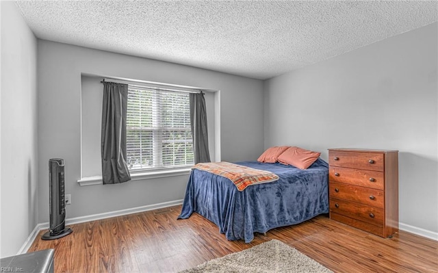 bedroom with a textured ceiling, baseboards, and wood finished floors