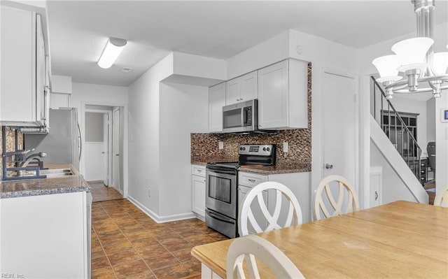 kitchen with decorative backsplash, appliances with stainless steel finishes, baseboards, a notable chandelier, and white cabinetry