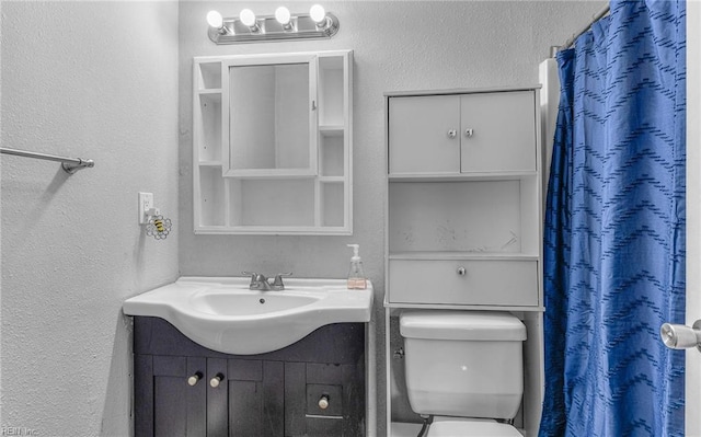 bathroom featuring vanity, a textured wall, and toilet