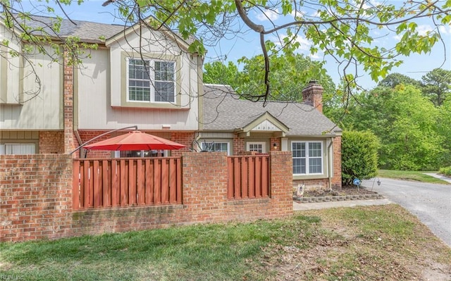 view of front of home featuring fence, a chimney, roof with shingles, and brick siding