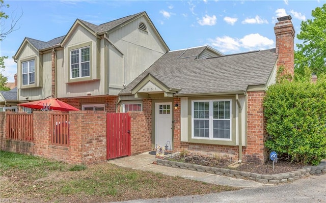 view of front facade with brick siding, a gate, fence private yard, and roof with shingles