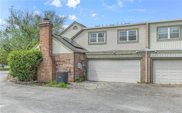 exterior space featuring a garage, a chimney, brick siding, central air condition unit, and driveway