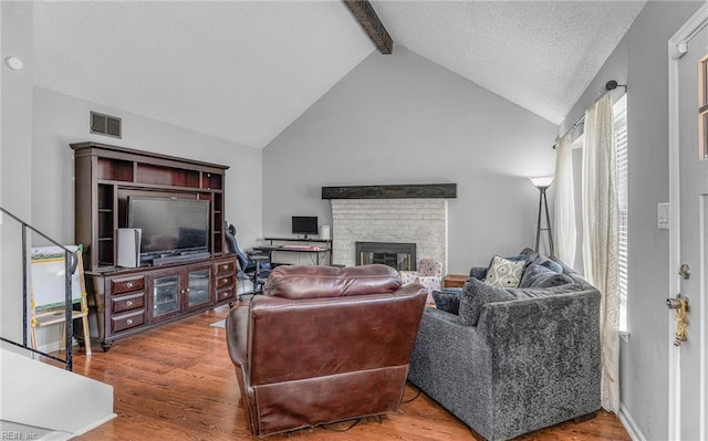 living room featuring visible vents, a brick fireplace, wood finished floors, beamed ceiling, and a textured ceiling