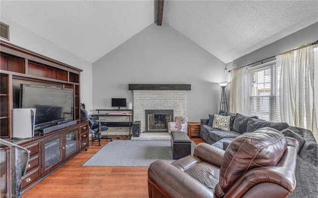 living area with a textured ceiling, beamed ceiling, a brick fireplace, and wood finished floors