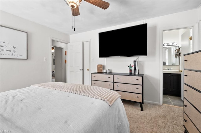 bedroom featuring baseboards, ceiling fan, light colored carpet, a sink, and ensuite bath