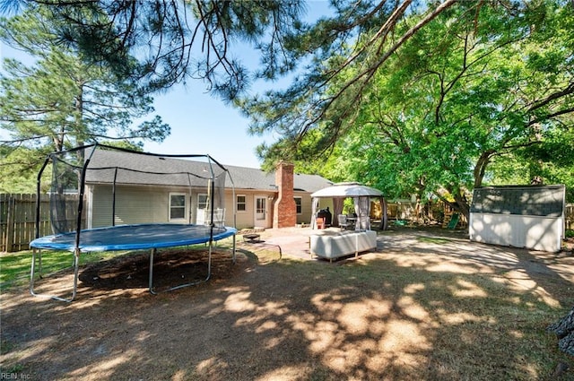 rear view of property with fence, a trampoline, a shed, an outbuilding, and a chimney