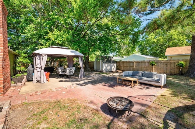 view of patio / terrace featuring an outdoor structure, an outdoor living space with a fire pit, a fenced backyard, a storage unit, and a gazebo