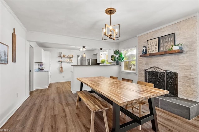 dining area featuring ornamental molding, a stone fireplace, wood finished floors, and a notable chandelier