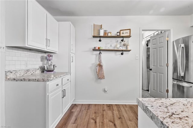 kitchen featuring freestanding refrigerator, baseboards, white cabinetry, light wood-style flooring, and backsplash