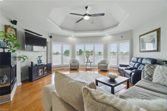 living area with light wood-style floors, a ceiling fan, a tray ceiling, and a healthy amount of sunlight