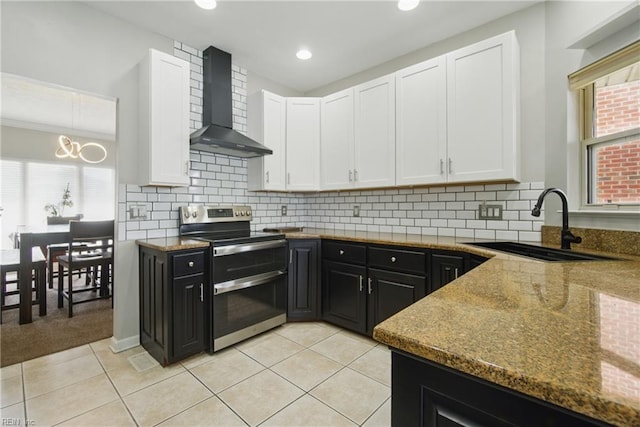 kitchen with wall chimney range hood, white cabinetry, double oven range, and a sink