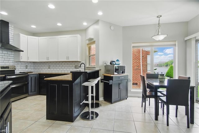 kitchen with a peninsula, wall chimney exhaust hood, white cabinetry, backsplash, and stainless steel appliances